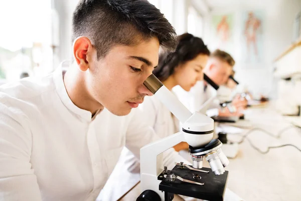 Belos alunos do ensino médio com microscópios em laboratório . — Fotografia de Stock