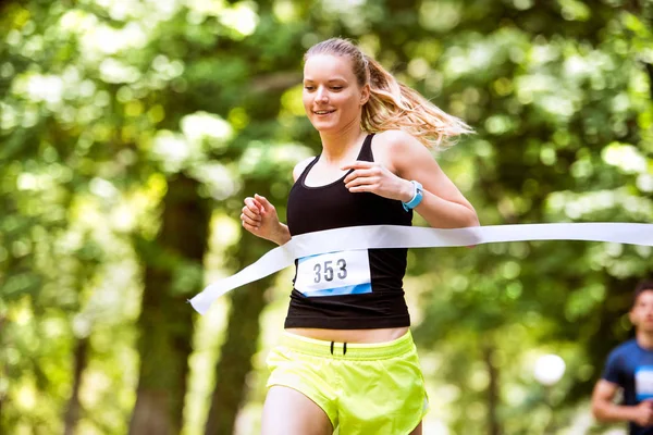 Νεαρή γυναίκα τρέχει στον αγώνα που διασχίζει τη γραμμή τερματισμού. — Φωτογραφία Αρχείου
