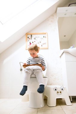 Tuvalette otururken tablet ile küçük kız.