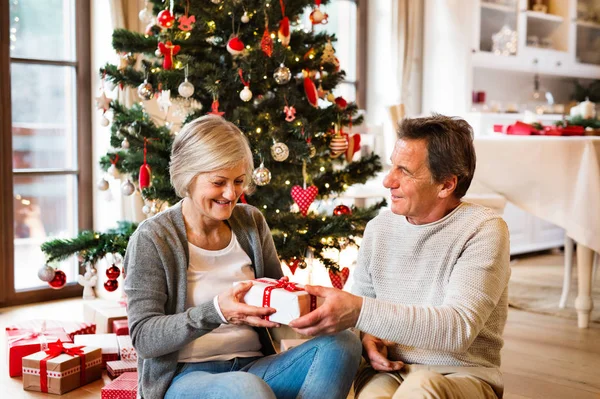 Pareja mayor frente al árbol de Navidad con regalos . — Foto de Stock