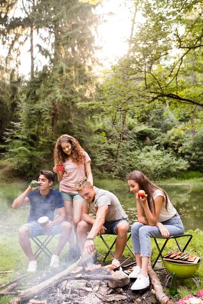 Tieners kamperen, koken van vlees op vreugdevuur. — Stockfoto