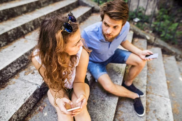 Jeune couple avec smartphones assis sur les escaliers en ville . — Photo