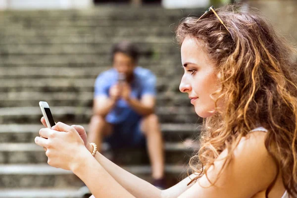 Unga par med smartphones som sitter på trappan i stan. — Stockfoto