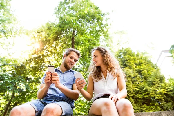 Jeune couple avec smartphones en ville assis sur un mur de béton . — Photo