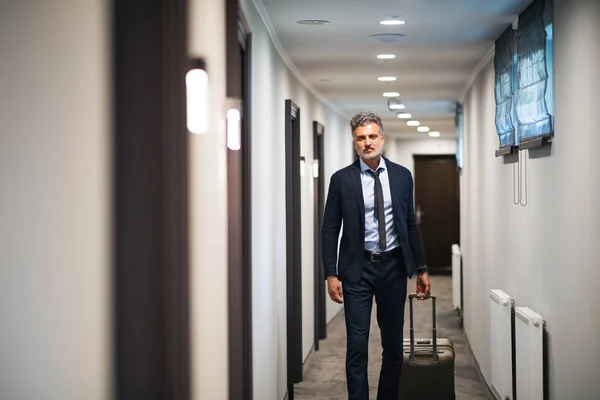 Uomo d'affari maturo che cammina con i bagagli in un corridoio d'albergo . — Foto Stock