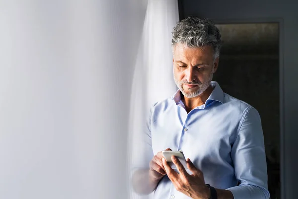 Uomo d'affari maturo con smartphone in una camera d'albergo . — Foto Stock