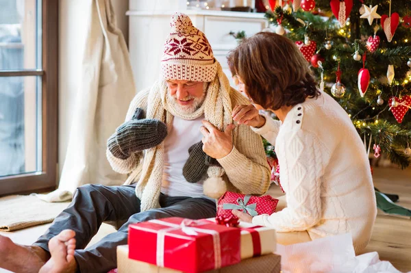 Äldre par framför julgranen njuter presenterar. — Stockfoto
