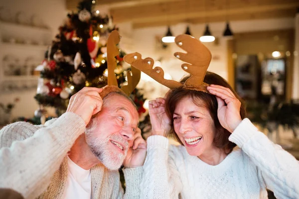 Senior couple in front of Christmas tree wearing deer antlers. — Stock Photo, Image