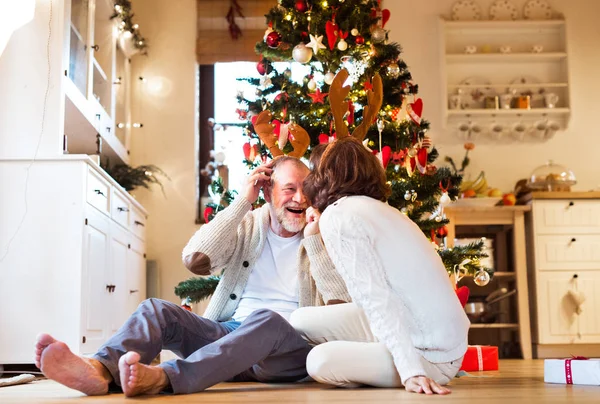 Senior couple in front of Christmas tree wearing deer antlers. — Stock Photo, Image