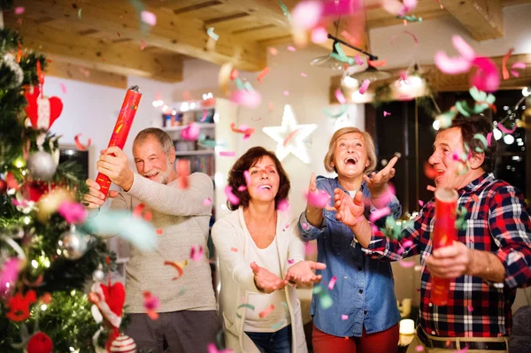 Amigos sênior com poppers confete ao lado da árvore de Natal . — Fotografia de Stock