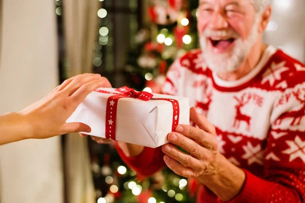 Senior man in front of Christmas tree holding a gift.