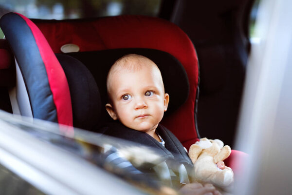 Little baby boy sitting in the car seat in the car.