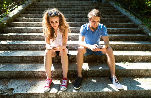 Pareja joven con smartphones sentados en las escaleras de la ciudad . — Foto de Stock