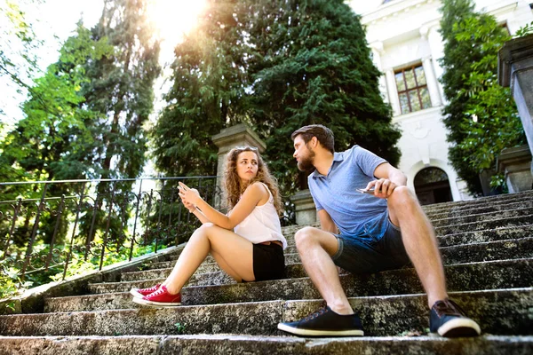 Young couple with smartphone sitting on stairs in town.