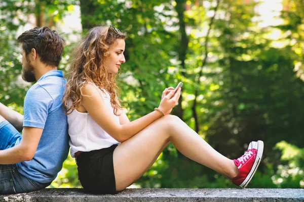 Молода пара зі смартфонами в місті, сидячи на бетонній стіні . — стокове фото