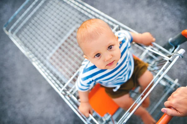 Chłopiec dziecko siedzi w wózek na zakupy poza. — Zdjęcie stockowe