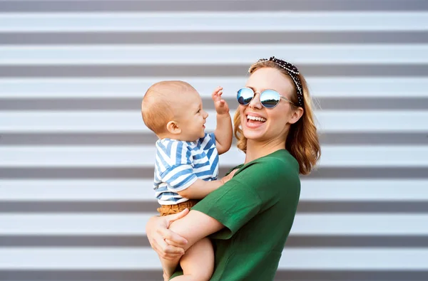 Jonge vrouw met een babyjongen permanent tegen de muur. — Stockfoto