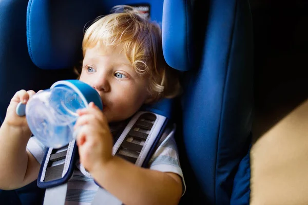 Little boy sitting in the car seat in the car, drinking. — Stock Photo, Image