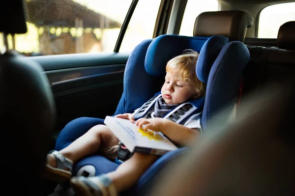 Mały chłopiec siedzi na siedzeniu samochodu, w samochodzie, trzyma książkę. — Zdjęcie stockowe