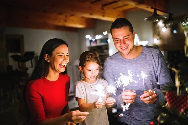 Mladá rodina s prskavky v době Vánoc doma. — Stock fotografie
