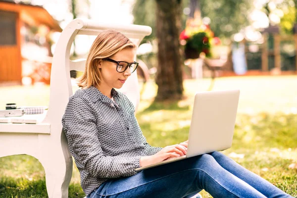 Jeune femme avec un ordinateur portable étudiant à l'extérieur . — Photo