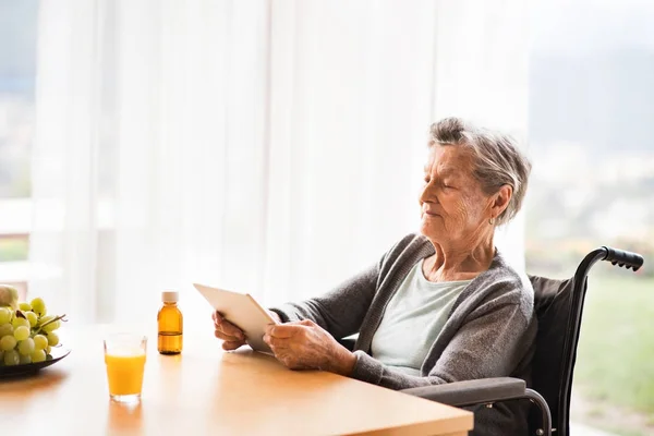 Mulher idosa em cadeira de rodas com tablet em casa . — Fotografia de Stock