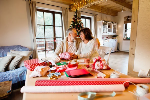 Casal sênior em camisolas embrulhando presentes de Natal juntos . — Fotografia de Stock