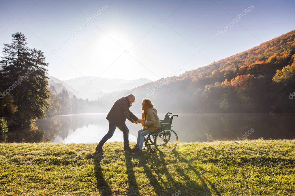 Senior couple with wheelchair in autumn nature.