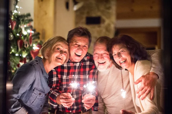 Amigos sênior com brilhos ao lado da árvore de Natal se divertindo . — Fotografia de Stock
