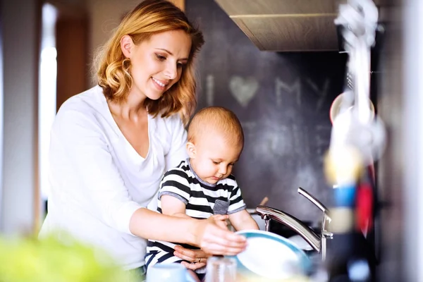 Jonge moeder met een babyjongen doen van huishoudelijk werk. — Stockfoto