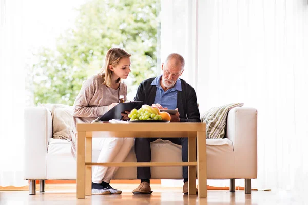 Salute visitatore e un uomo anziano con tablet durante la visita a casa . — Foto Stock