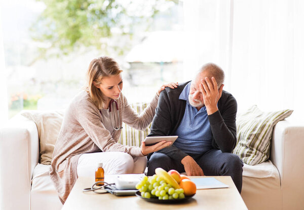 Health visitor and a senior man with tablet during home visit.