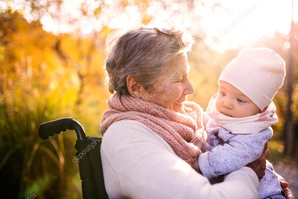 An elderly woman in wheelchair with baby in autumn nature.