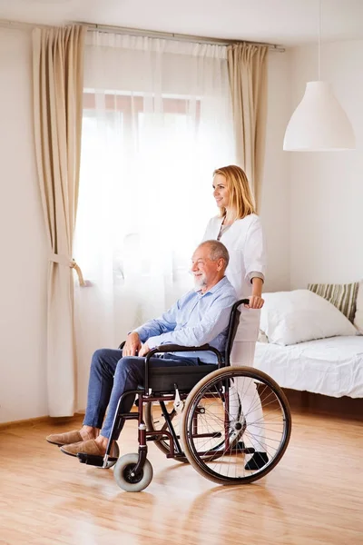 Медсестра і старший чоловік в інвалідному візку під час домашнього візиту . — стокове фото