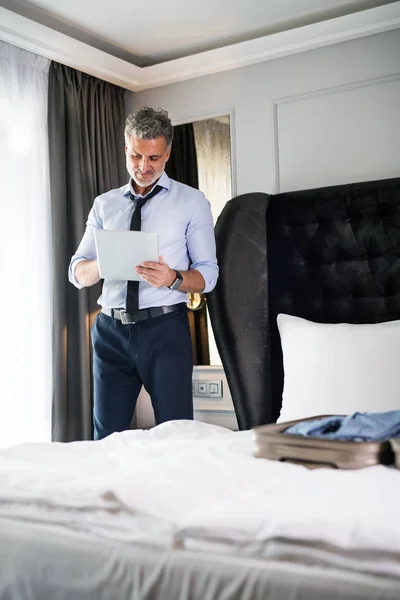 Maduro hombre de negocios con tableta en una habitación de hotel . — Foto de Stock