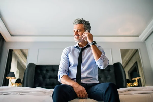 Rijpe zakenman met smartphone in een hotelkamer. — Stockfoto