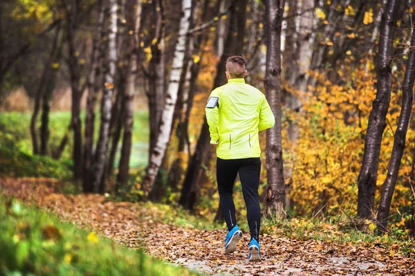 Jovem atleta com smartphone correndo no parque no outono . — Fotografia de Stock