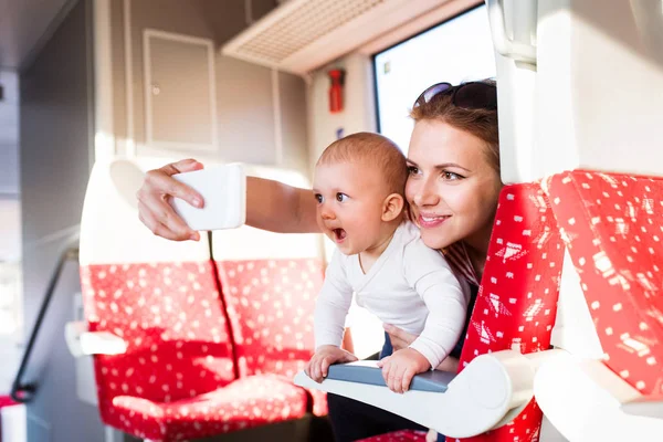 Mladá matka s smartphone cestování vlakem s dítětem. — Stock fotografie