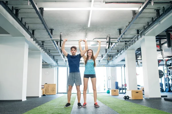 Jeune couple en forme dans la salle de gym levant haltère lourde . — Photo