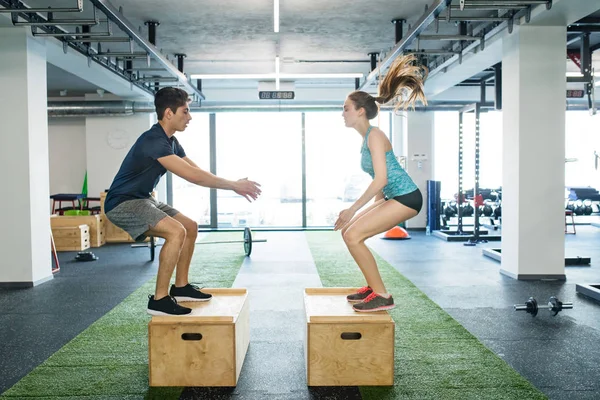 Jeune couple en forme faisant de l'exercice dans la salle de gym, faisant des sauts de boîte . — Photo
