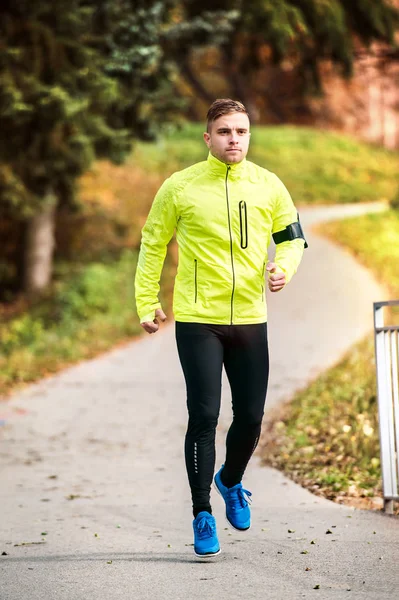 Joven atleta con smartphone corriendo en el parque en otoño . —  Fotos de Stock