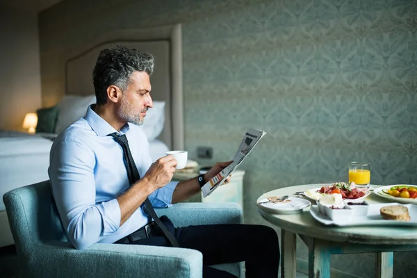 Mature businessman having breakfast in a hotel room. — Stock Photo, Image