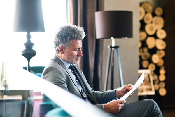 Mature businessman reading in a hotel lounge. — Stock Photo, Image