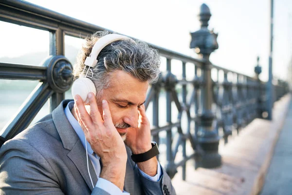 Mature businessman with headphones in a city. — Stock Photo, Image