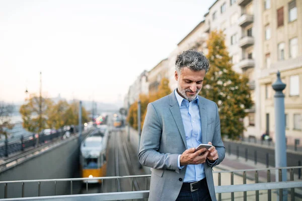 Mature businessman with a smartphone in a city. — Stock Photo, Image