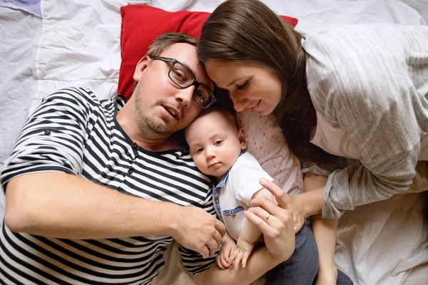 Bela família jovem com pequeno filho deitado na cama . — Fotografia de Stock