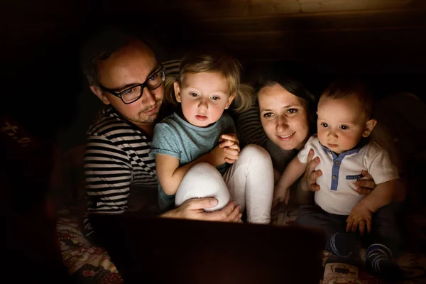 Padres jóvenes con niños pequeños y portátil por la noche . — Foto de Stock