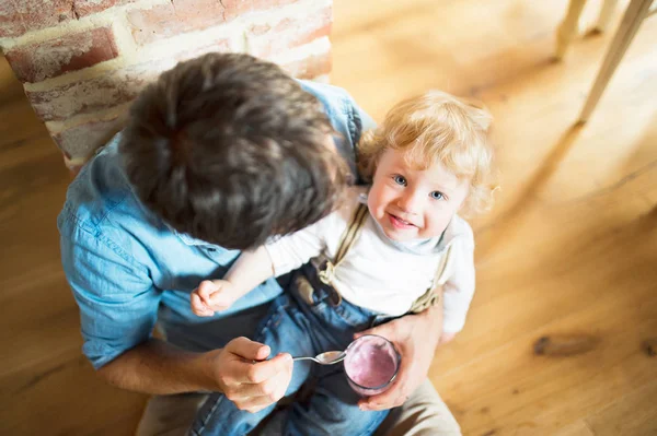 Giovane padre a casa nutrire il suo piccolo figlio con yogurt . — Foto Stock