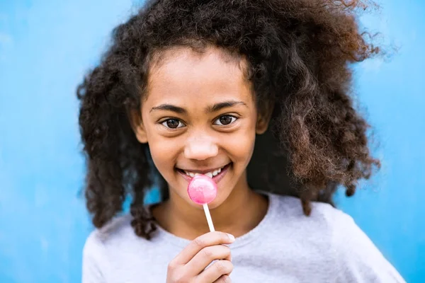 Afroamericano ragazza con ricci capelli all'aperto mangiare lecca-lecca . — Foto Stock