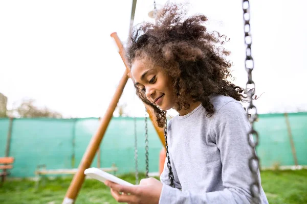 Akıllı telefon mesaj ile salıncak üzerinde Afro-Amerikan kız. — Stok fotoğraf